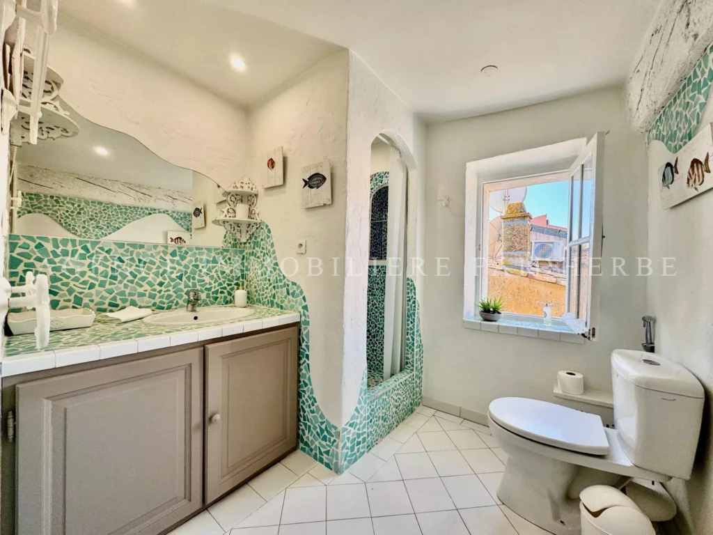 Belle salle de bain lumineuse avec des mosaïques vertes et un espace ensoleillé.