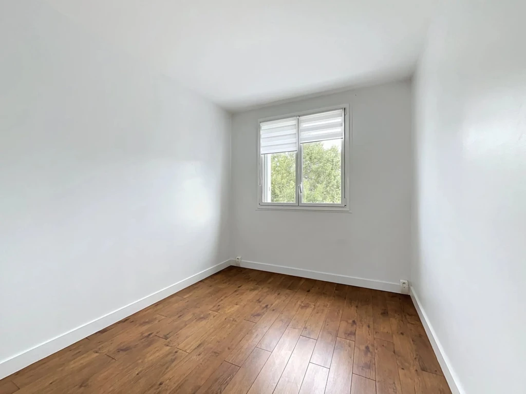 Chambre lumineuse avec parquet en bois et fenêtre offrant une vue sur la jardin.