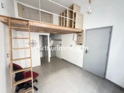 Un petit appartement avec une mezzanine en bois, une échelle, et une cuisine ouverte.