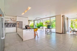 Une cuisine moderne et spacieuse avec un îlot central, de grandes fenêtres, et une vue sur le jardin.