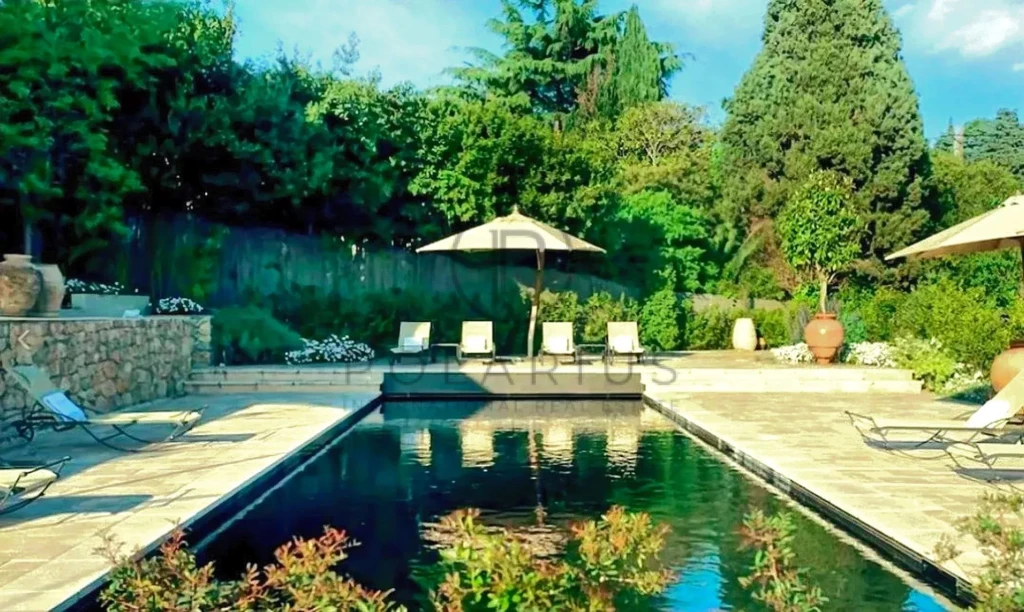 Une piscine entourée de chaises longues et de parasols, avec une végétation luxuriante en arrière-plan.