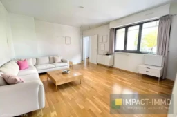 Grand salon lumineux avec parquet en bois et grandes fenêtres offrant une belle vue.