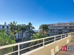 Vue depuis un balcon avec des palmiers et des bâtiments résidentiels sous un ciel bleu.