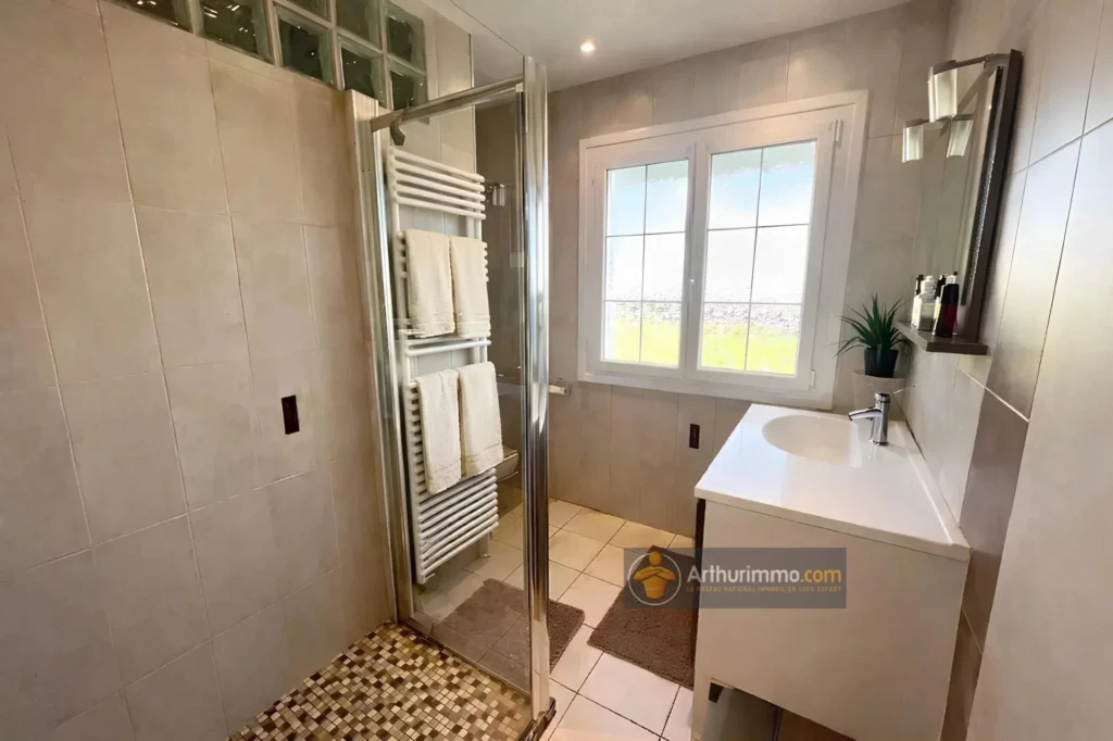 Salle de bain moderne avec douche, lavabo et fenêtres lumineuses.