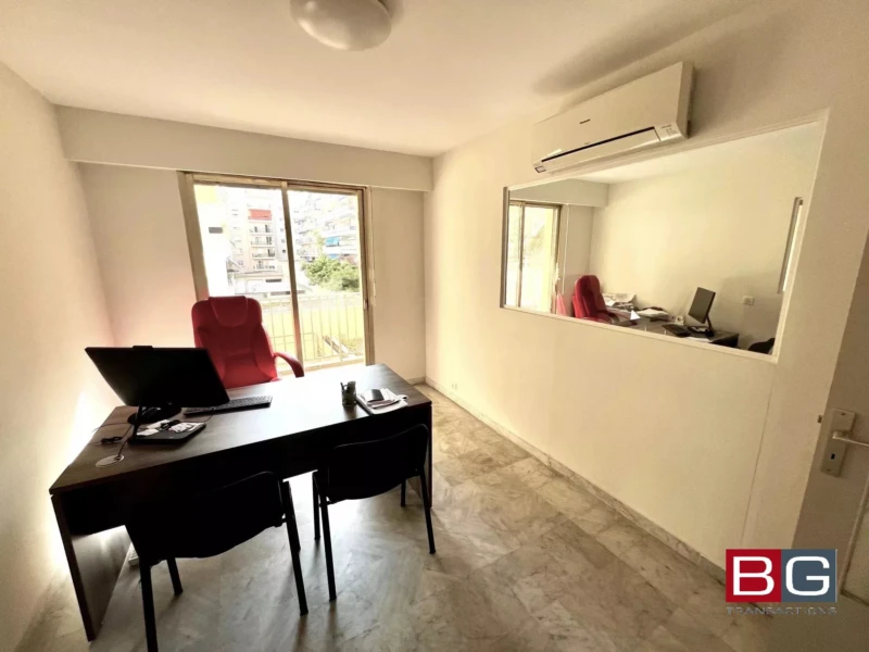 Un bureau spacieux avec un grand bureau, une chaise rouge, un ordinateur portable et une climatisation sur le mur. Une grande fenêtre illumine la pièce.