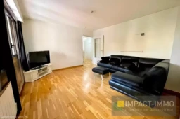 Salon lumineux avec un canapé en cuir noir et une télévision moderne.