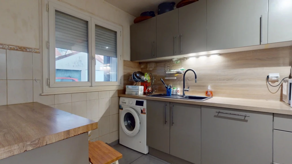 Petite cuisine moderne avec des placards gris, un évier, une machine à laver et un plan de travail en bois.