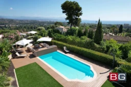 Vue d'une piscine entourée de verdure avec des transats et des parasols, offrant un panorama sur la campagne environnante et la mer.