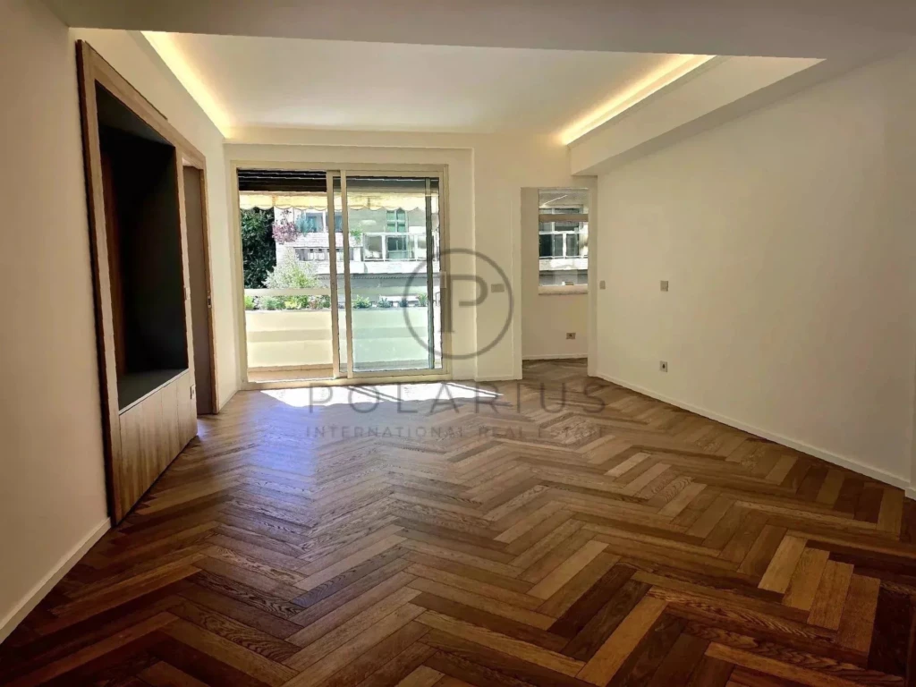 Une pièce lumineuse avec un parquet en chevron et une grande baie vitrée.