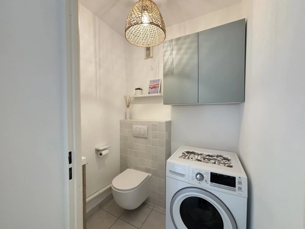 Toilettes indépendantes suspendues aménagées avec un espace buanderie pour la machine à laver.