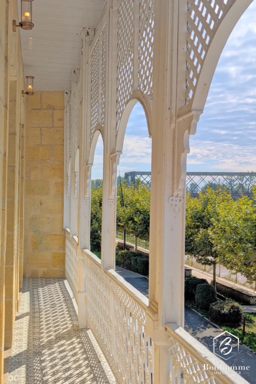 Balcon en bois sculpté avec vue sur un jardin verdoyant et ciel bleu.