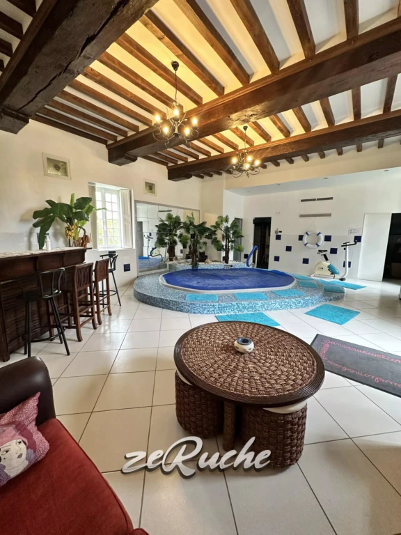 Salon lumineux avec piscine intérieure et plafond en bois apparentes, idéal pour la détente.