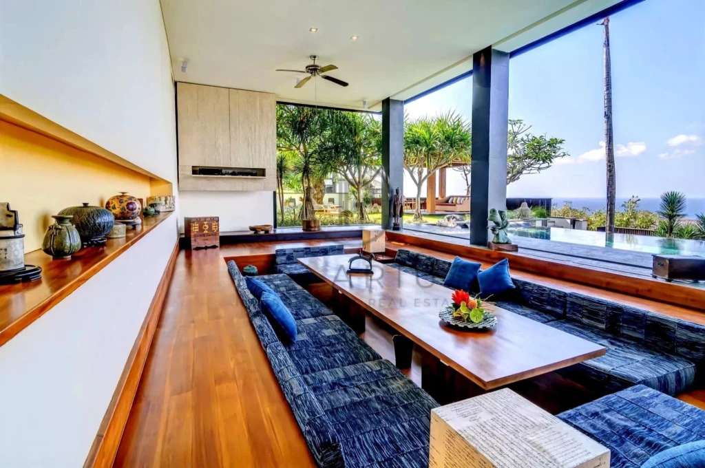 Salle de séjour moderne avec de grandes baies vitrées, une table basse en bois entourée de canapés, offrant une vue sur la piscine et le jardin extérieur.
