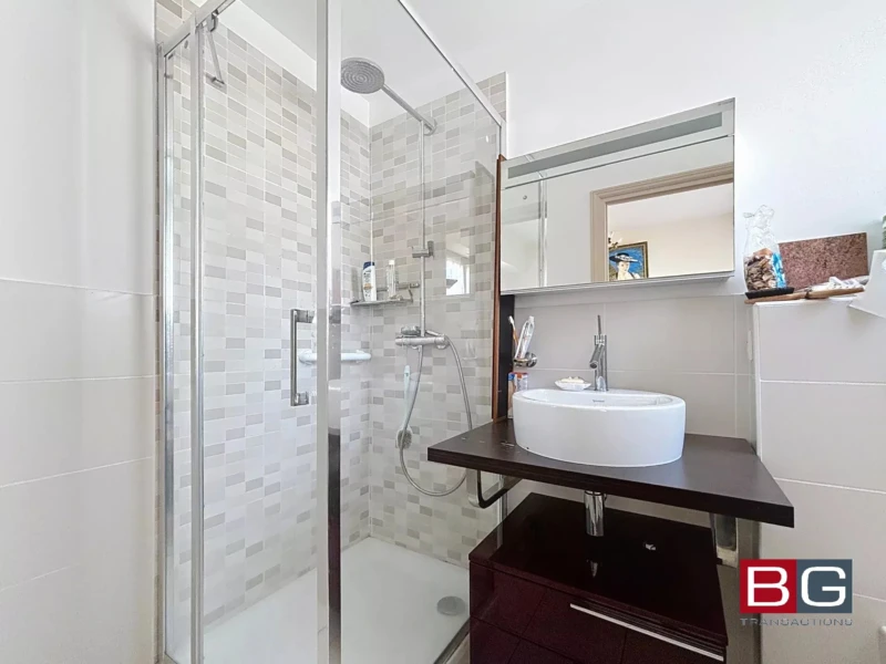 Une salle de bains moderne avec une douche vitrée et un lavabo sur une étagère en bois sombre.