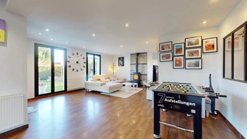 Un salon moderne avec un sol en bois, un canapé blanc, une table de baby-foot et des œuvres d'art accrochées au mur.