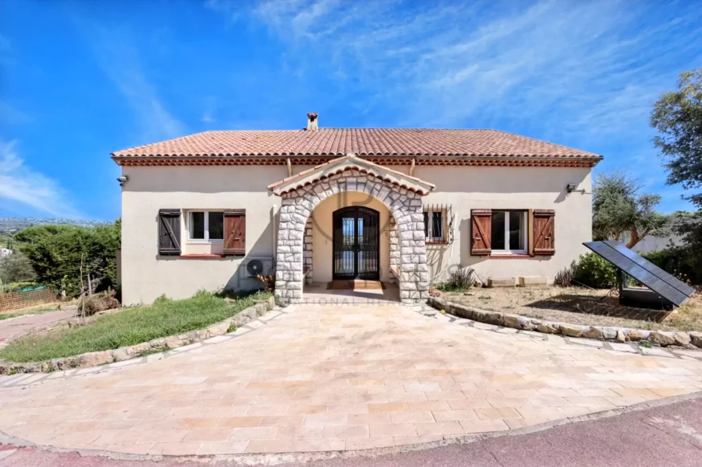 Une maison méditerranéenne avec un toit en tuiles, entourée de végétation, sous un ciel bleu.