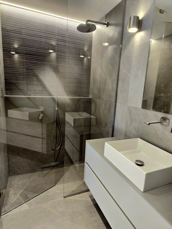 Une salle de bain moderne avec une douche en verre, un lavabo blanc et un éclairage contemporain.