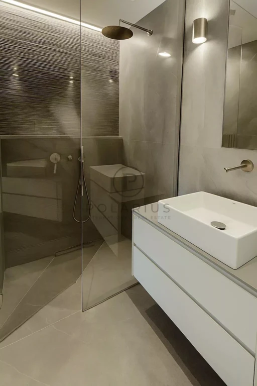 Une salle de bain moderne avec une douche en verre, un lavabo carré sur un meuble blanc, et des murs en béton poli.