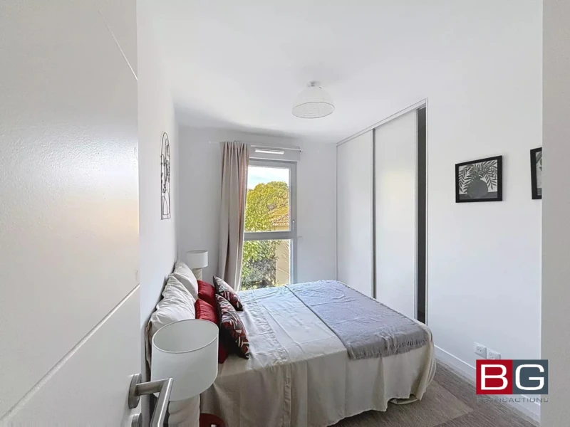 Une chambre lumineuse avec un lit double, des rideaux beiges et des tableaux encadrés sur les murs blancs.